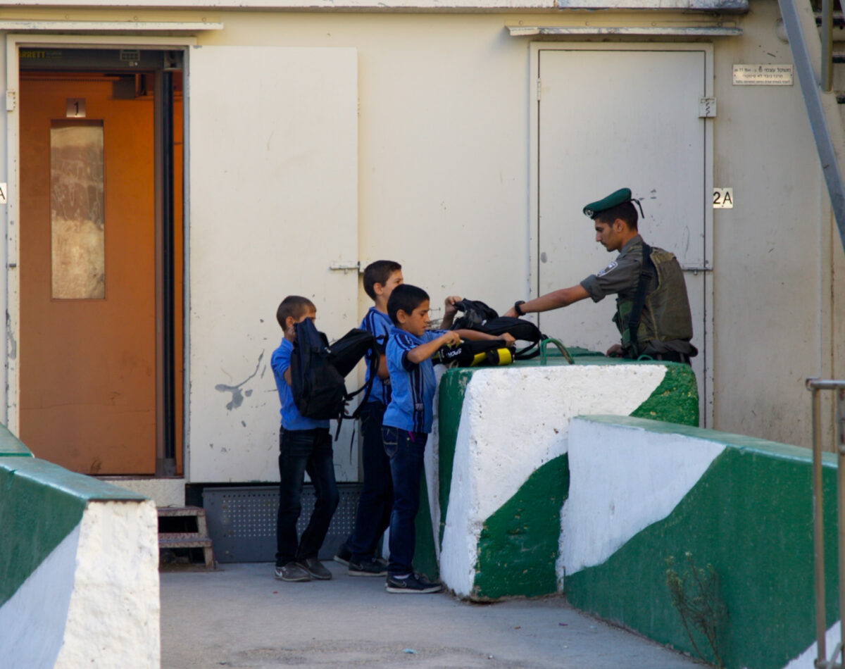 Israeli soldiers search the school bags at a checkpoint in Hebron