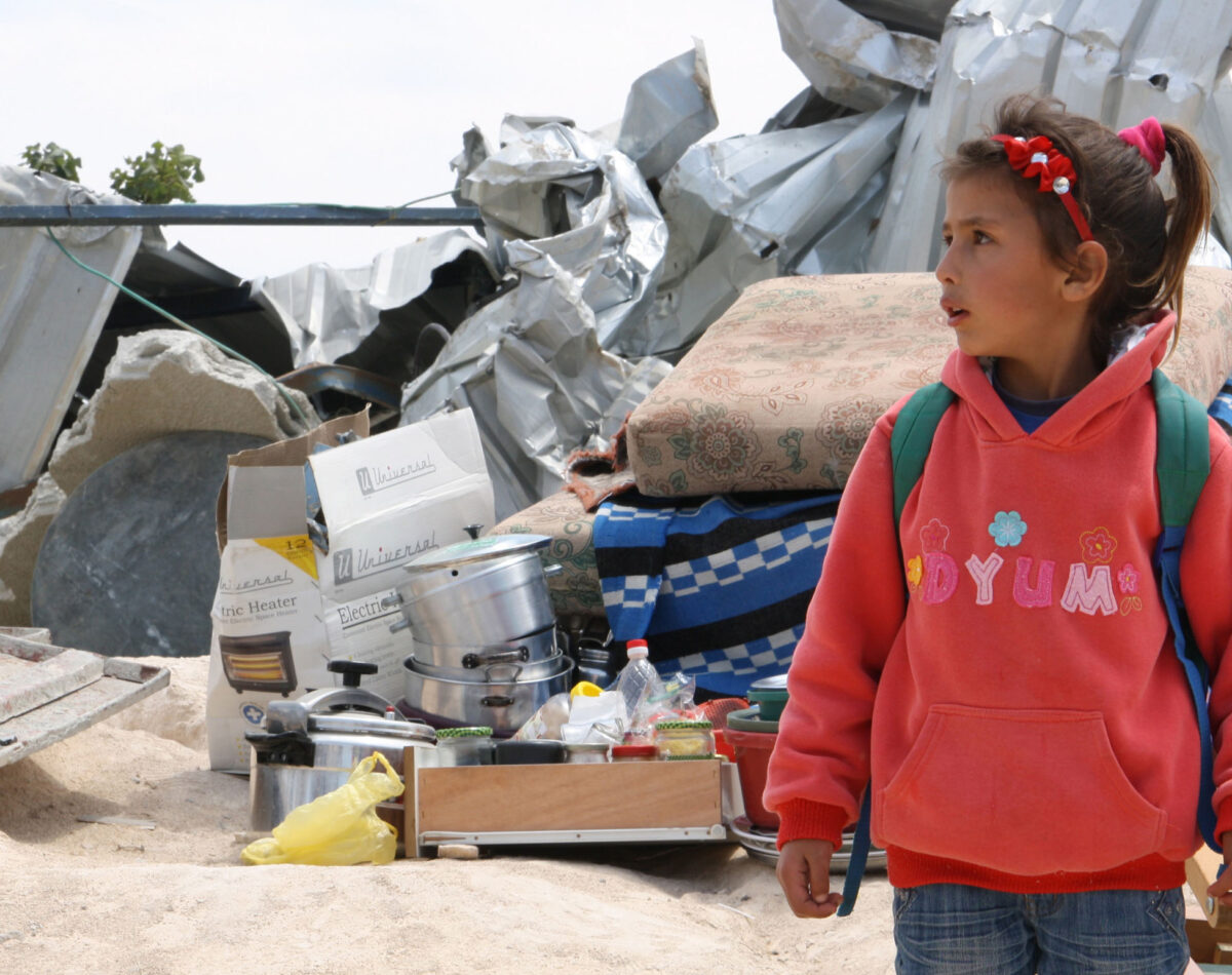 A Palestinian child stands in front of his belongings salvaged from his home in the before it was demolished
