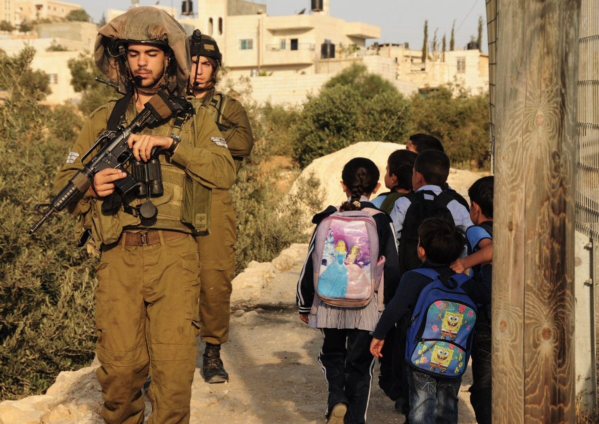 Palestinian children walks past soldiers on the way to school