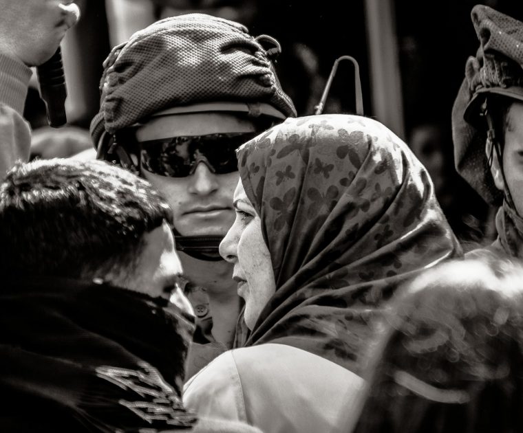 A Palestinian woman waits at a checkpoint next to Israeli soldiers