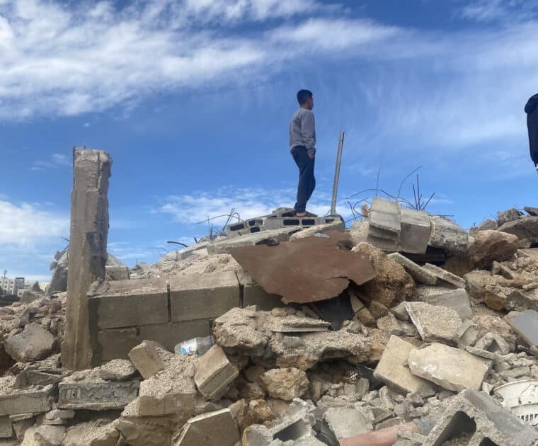 Boy stands on top of rubble of his home
