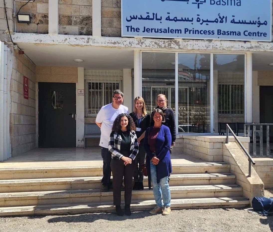 EAPPI visit to JPBC Five people (EAPPI human rights monitors and staff from the Centre) standing on the staircase in front of the center. You can see the sign for the center in the back with the name in arabic too 'The Jerusalem Princess Basma Centre'.
