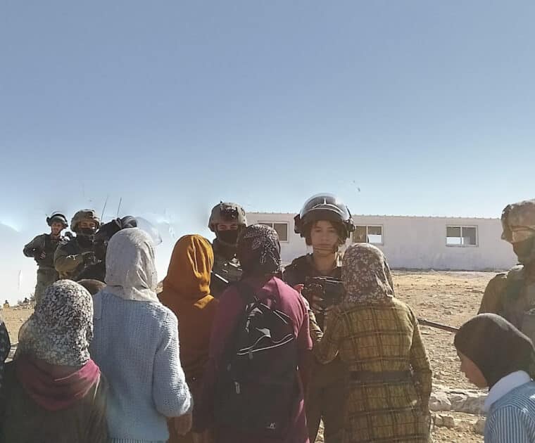 Palestinian women with hijabs facing Israeli soldiers. One solider is a young woman too.