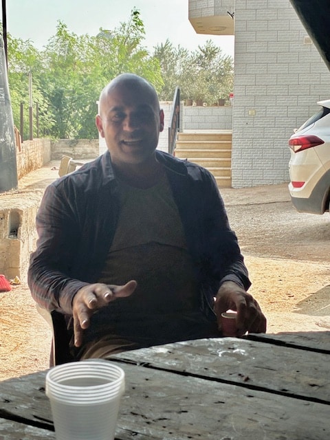 Photo of a man smiling sitting at a table having tea during the day.
